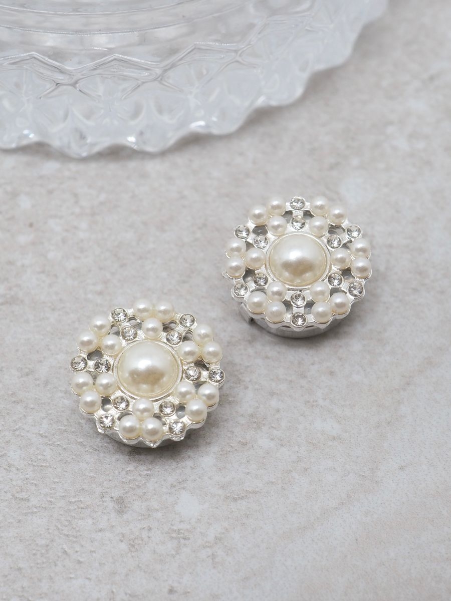 Denne delikate knappepynten er formet som en blomst og gir et feminint og sofistikert preg til plaggene dine. De blanke glassperlene og perlene, gir et klassisk og tidløst uttrykk.