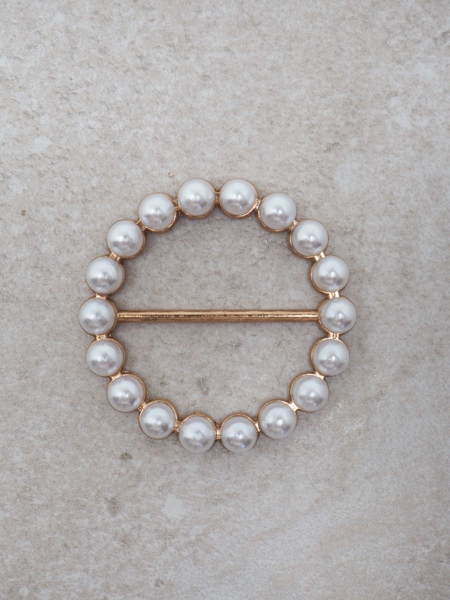 Denne gullfargede skjerfnålen er formet som en rund ring (ca. 4x3 cm) og dekorert med delikate perler som gir et feminint og elegant uttrykk.