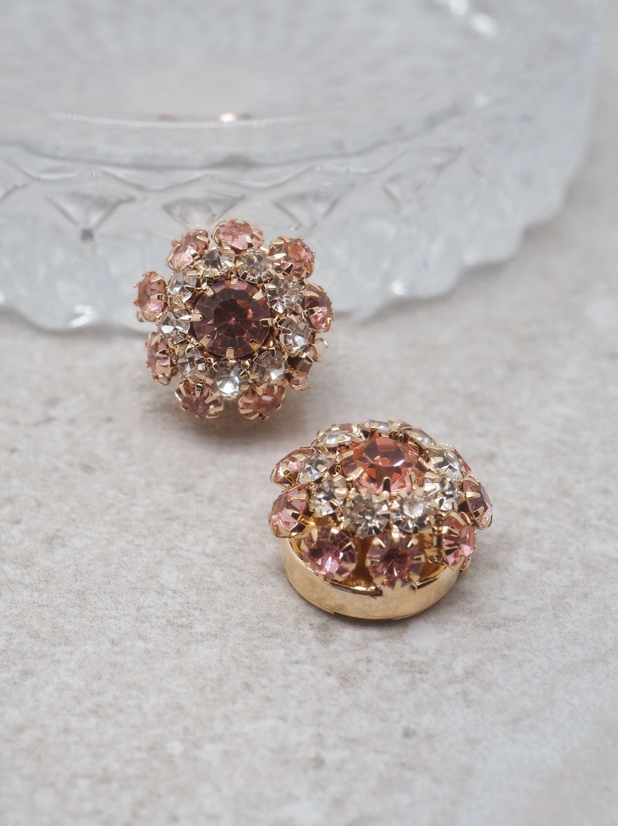 Løft antrekket med denne vakre knappepynten i gullfarge formet som en blomst, dekorert med glitrende rosa og blanke glassteiner. Perfekt til å skjule knapper på skjorter eller gensere, og gir et feminint og elegant uttrykk.