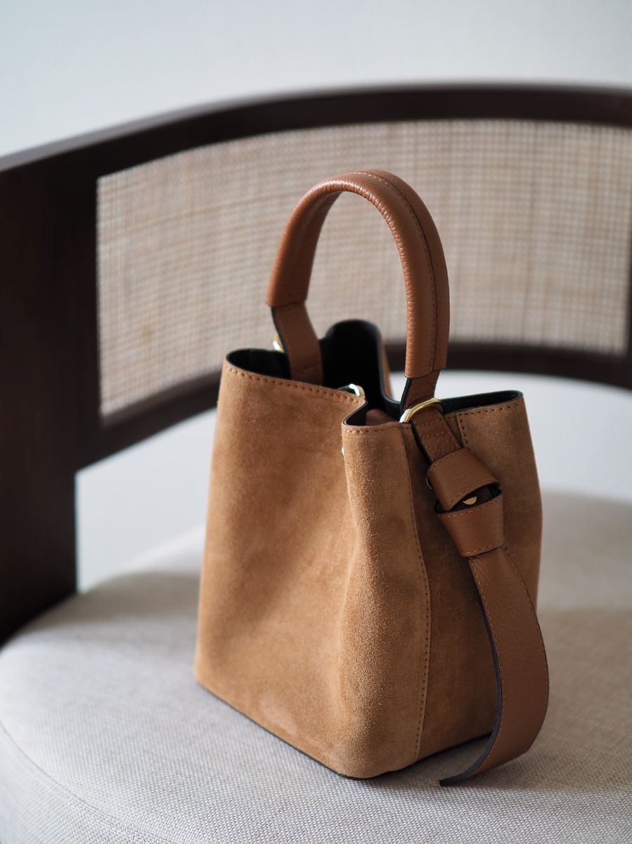 Sofistikert og elegant bøtteveske i både semsket og glatt skinn. Vesken har et dekorativt knutebelte. Vesken har to stropper, den lengste er regulerbar, den andre er et håndtak.