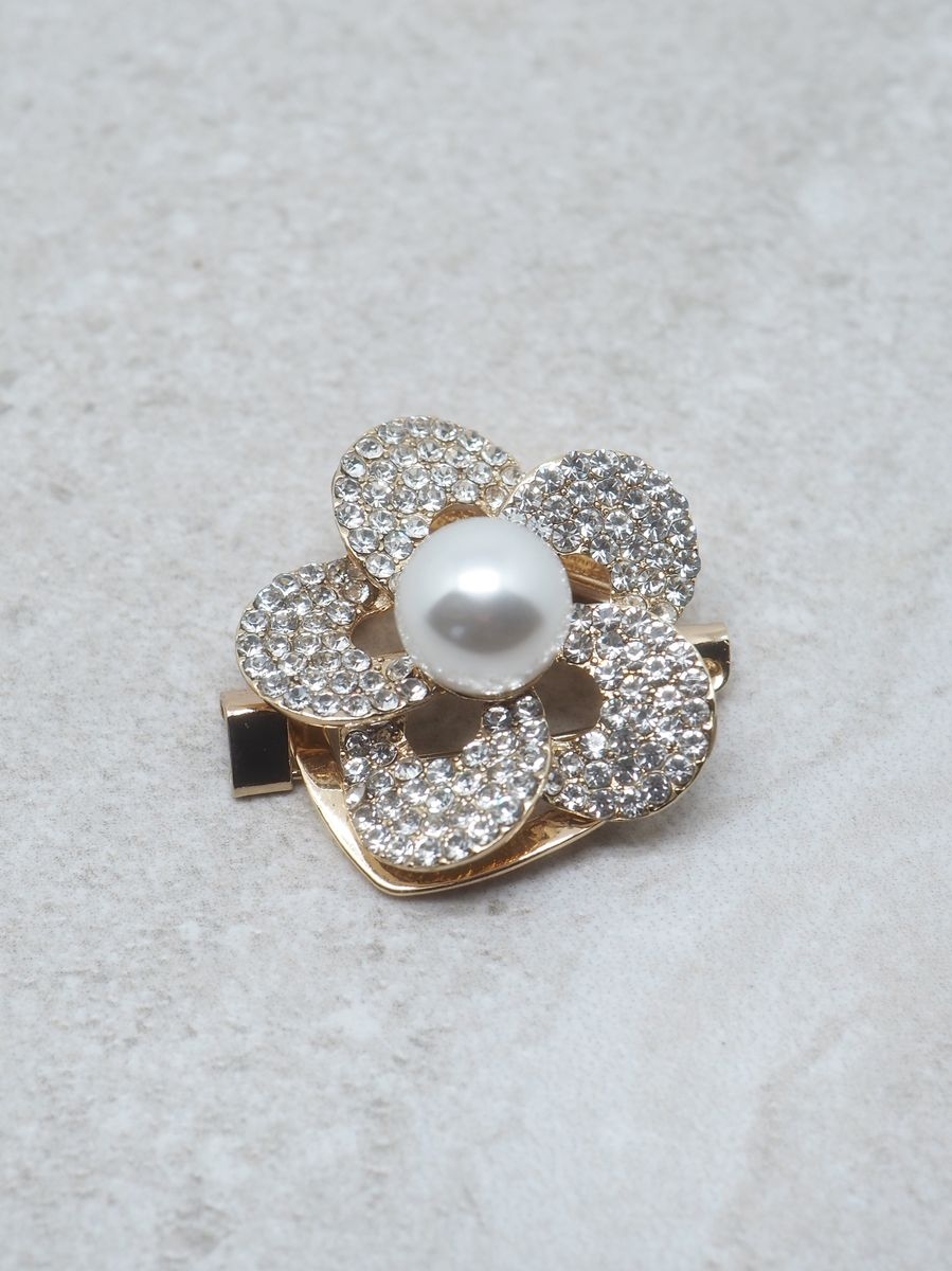 Denne vakre skjerfnålen er formet som en blomst og gir et elegant og feminint uttrykk til antrekket ditt. De blanke glassperlene fanger lyset på en diskret og eksklusiv måte, mens perlen i midten gir et klassisk og tidløst preg.