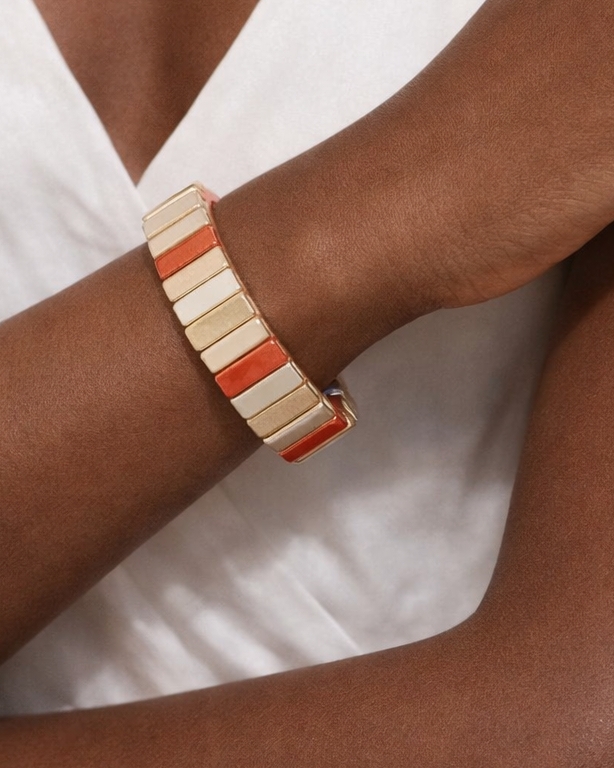 Emaljert strikkarmbånd i korall, gull og beige fargekombinasjoner. Bredde ca 1,7cm. Nikkelfritt produkt.