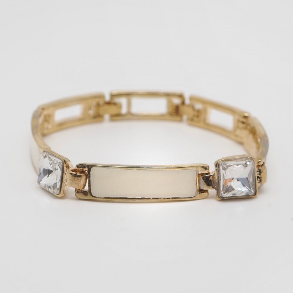 Armbånd i gullfarge med firkantete krystaller og emaljerte detaljer i off-white.

Nikkelfritt.
