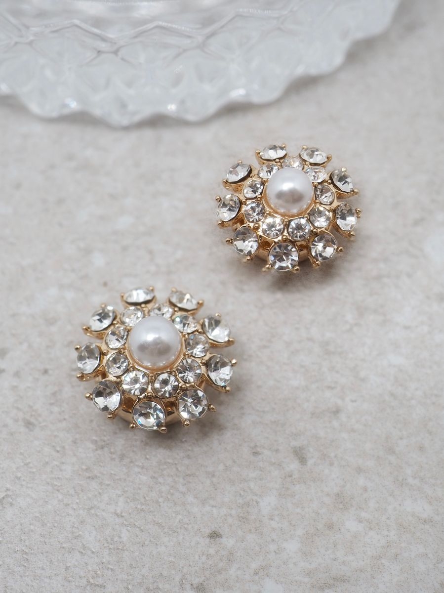 Denne delikate knappepynten er formet som en blomst og gir et feminint og sofistikert preg til plaggene dine. De blanke glassperlene gir et vakkert spill i lyset, mens perlen i midten tilfører et klassisk og tidløst uttrykk.