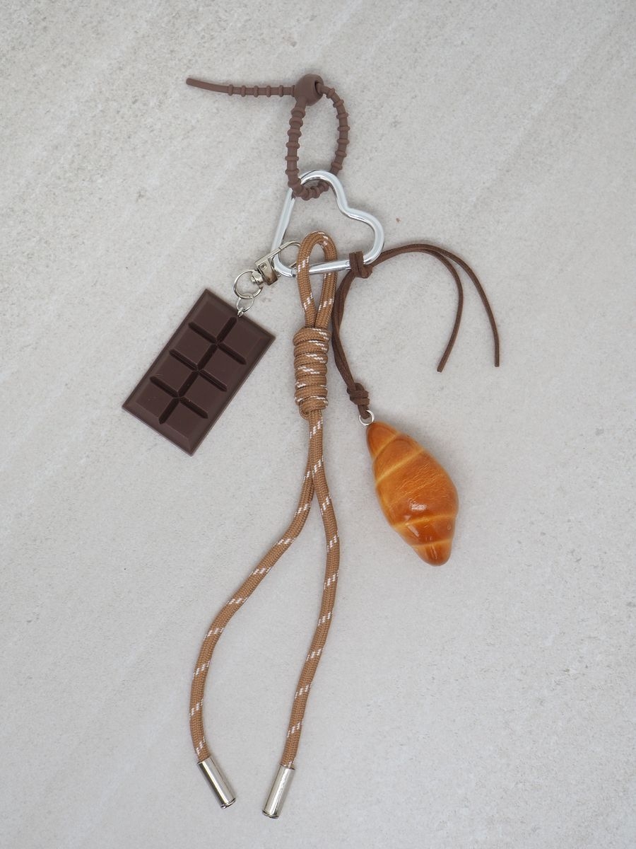 Fresh opp vesken din med veskepynt med brunt tau og croissant + sjokolade. Pynten har sølvdetaljer.

Lende ca 23cm