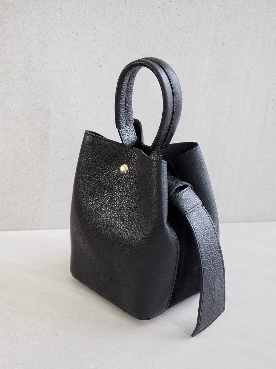 Sofistikert og elegant bøtteveske i både semsket og glatt skinn. Vesken har et dekorativt knutebelte. Vesken har to stropper, den lengste er regulerbar, den andre er et håndtak.