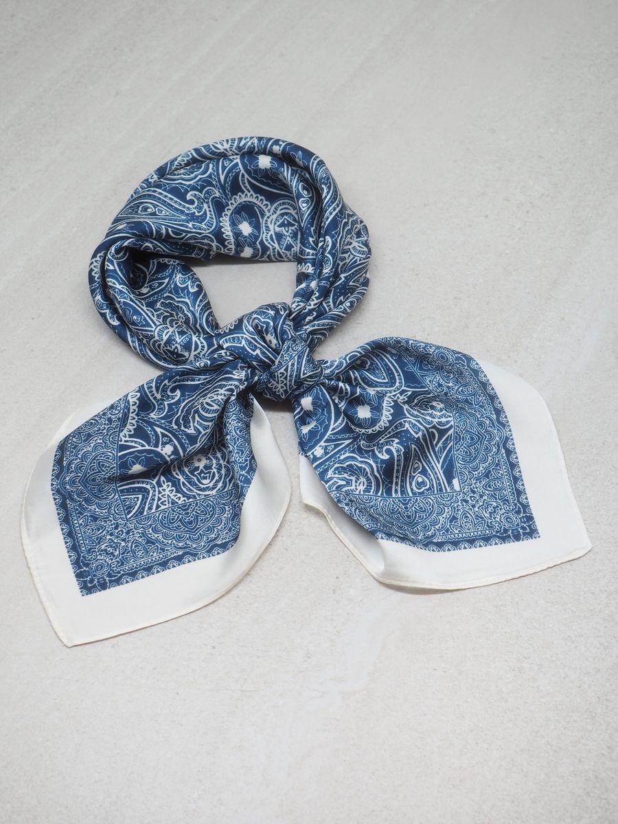 Dette klassiske satengskjerfet i mørkeblå og off-white er et tidløst tilbehør som gir antrekket et elegant og gjennomført uttrykk. Den rolige og stilrene fargekombinasjonen gjør skjerfet lett å kombinere med både lyse og mørke plagg.