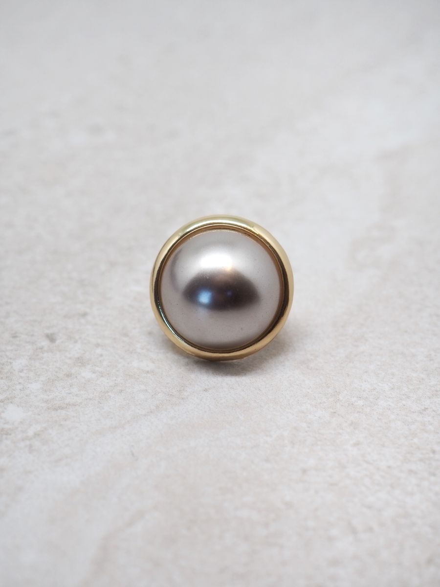 Denne elegante skjerfnålen i gullfarge med en vakker, glansfull perle i beige, gir antrekket et sofistikert og feminint uttrykk. Den er liten og nett (ca. 2,5x2,5 cm), men likevel et blikkfang som løfter både skjerf, sjal og yttertøy.