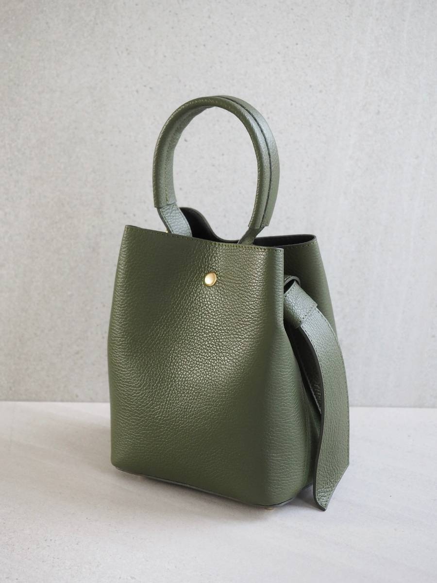 Sofistikert og elegant bøtteveske i både semsket og glatt skinn. Vesken har et dekorativt knutebelte. Vesken har to stropper, den lengste er regulerbar, den andre er et håndtak.
Vesken lukkes med magnet og karabinkrok.