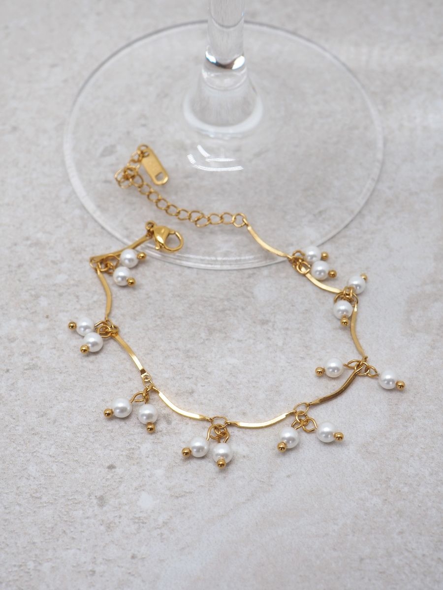 Dette elegante armbåndet kombinerer en fin gullfarget lenke med små, delikate perlecharms som beveger seg lett rundt håndleddet. 