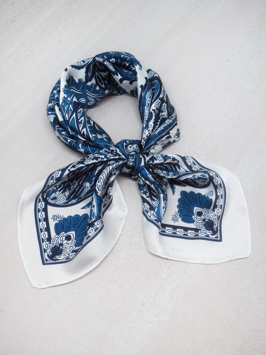 Dette klassiske satengskjerfet i blå og off-white er et tidløst tilbehør som løfter ethvert antrekk. De rolige og elegante fargene gjør skjerfet enkelt å kombinere med både lyse og mørke plagg, og det passer like godt til hverdagsbruk som til fest.